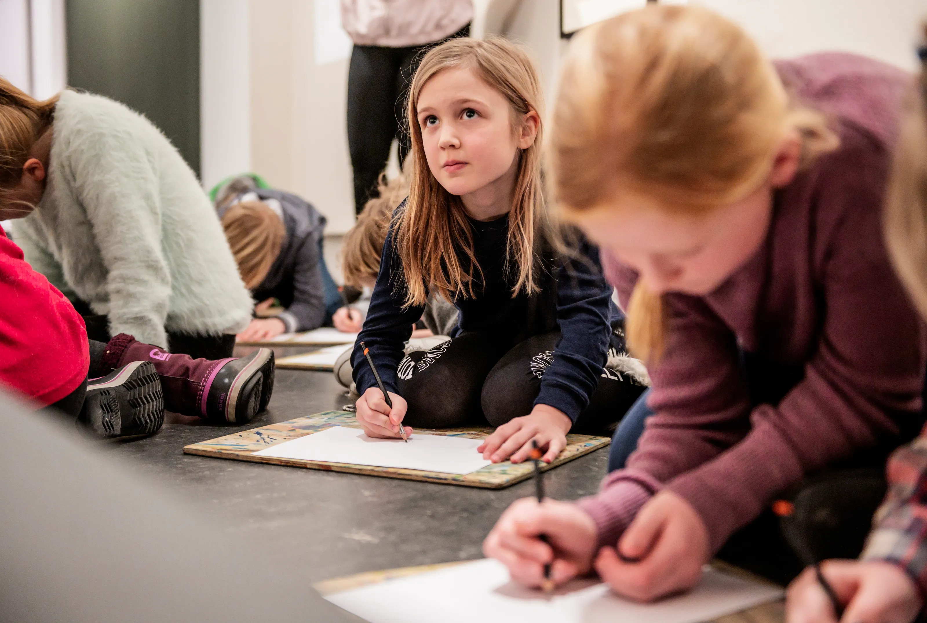 Elever som tegner på tegnebrett på gulvet