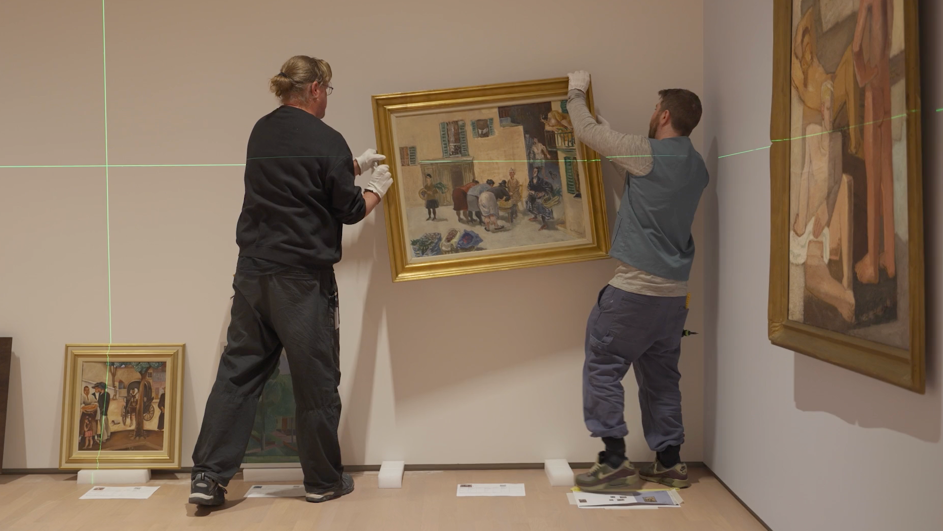 To montører henger opp maleri i utstillingen